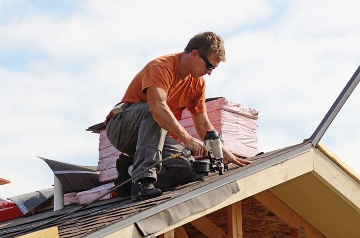 roofing expert putting the asphalt roofing on a large commercial apartment building